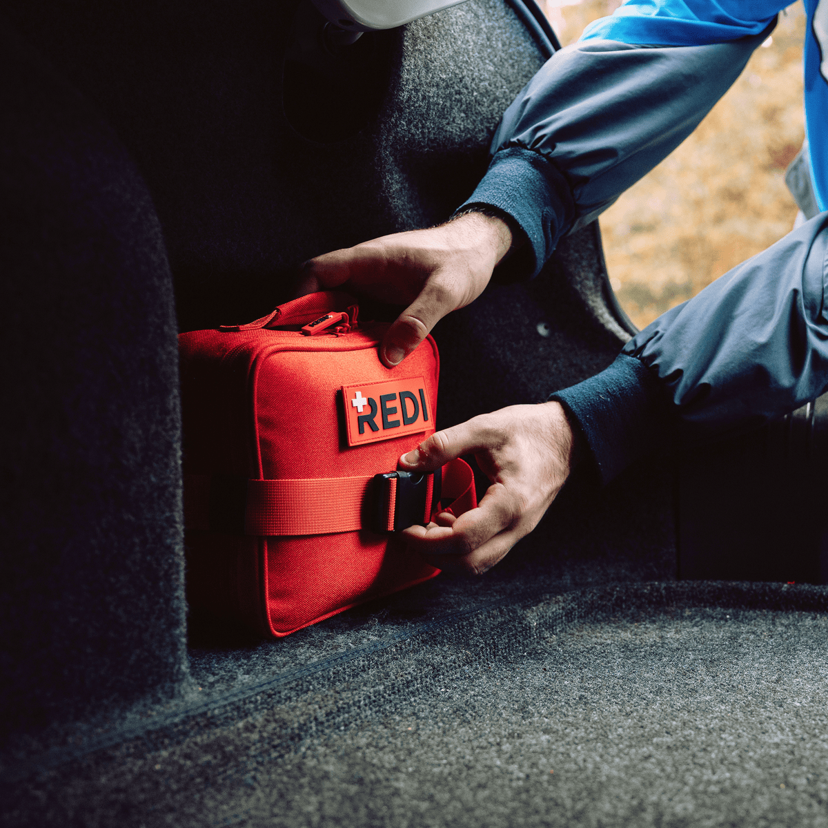 Driver securing The Roadie car emergency kit to the carpeted trunk with its mounting strap