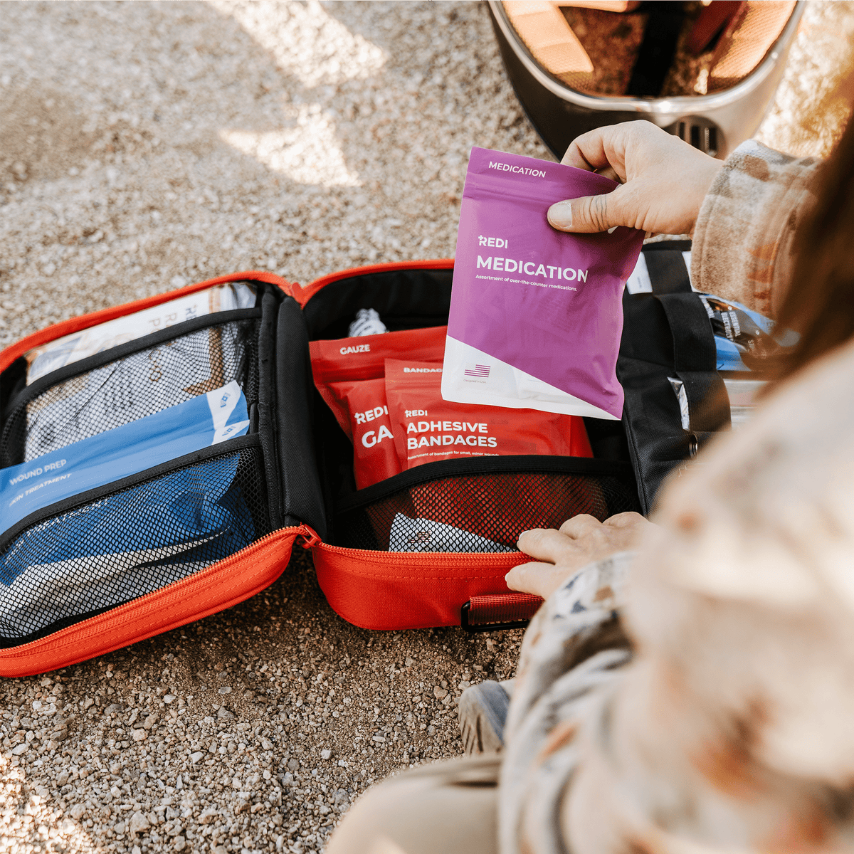 Person pulling the labeled medication pouch from an open Roadie car first aid kit outdoors