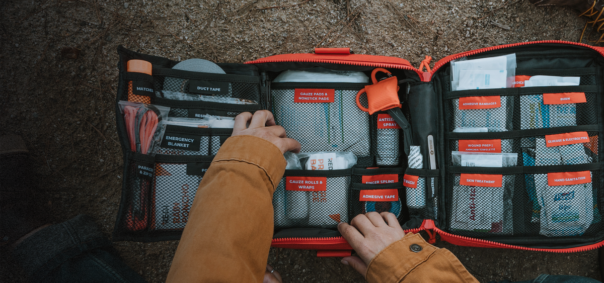 A photo of the Roadie open, its labeled pouches for each first aid item, and hands digging in to grab gauze rolls. 